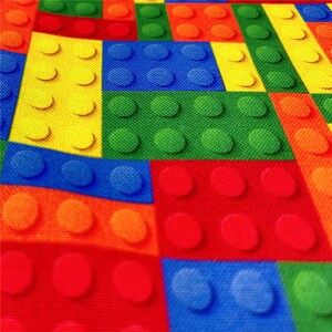 K&ouml;nnte beinhalten: Ein farbenfroher Stoff mit einem sich wiederholenden Muster aus ineinandergreifenden Quadraten. Jedes Quadrat hat eine andere Farbe und ist so gestaltet, dass es wie ein Lego-Stein aussieht. Die Farben sind Rot, Orange, Gelb, Gr&uuml;n, Blau und Hellblau.