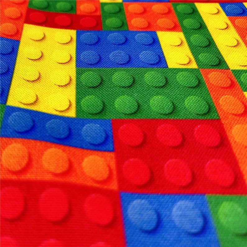 K&ouml;nnte beinhalten: Ein farbenfroher Stoff mit einem sich wiederholenden Muster aus ineinandergreifenden Quadraten. Jedes Quadrat hat eine andere Farbe und ist so gestaltet, dass es wie ein Lego-Stein aussieht. Die Farben sind Rot, Orange, Gelb, Gr&uuml;n, Blau und Hellblau.