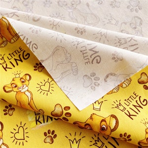 Puede incluir: Tela amarilla con un patr&oacute;n repetido de un cachorro de le&oacute;n de dibujos animados, huellas de patas, corazones y coronas. La tela tiene el texto "My Little King" repetido en toda su superficie.
