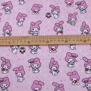 May include: Pink fabric with a repeating pattern of a cartoon bunny holding a strawberry. The bunny is wearing a pink dress and a white bow. The background is a light pink with white polka dots.