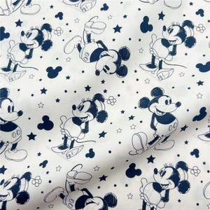 Könnte beinhalten: Weißer Stoff mit einem sich wiederholenden Muster von Mickey und Minnie Mouse in Marineblau. Das Design umfasst Sterne, Mickey Mouse-Silhouetten und kleine Blumenformen. Die Zeichentrickfiguren sind in verschiedenen Posen.