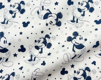 Op de afbeelding: Witte stof met een herhalend patroon van Mickey en Minnie Mouse in marineblauw. Het ontwerp bevat sterren, Mickey Mouse-silhouetten en kleine bloemvormen. De stripfiguren staan in verschillende poses.