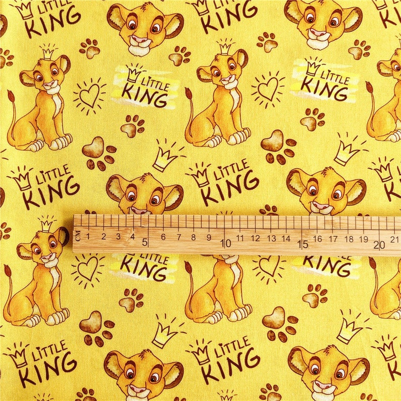 Puede incluir: Tela amarilla con un patr&oacute;n repetido de un cachorro de le&oacute;n de dibujos animados con una corona, huellas de patas, corazones y el texto "Little King".
