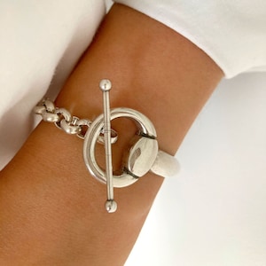 Op de afbeelding: Een zilveren armband met een grote, ronde toggle-sluiting. De armband is gemaakt van een kettinglink-ontwerp.