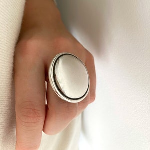 Peut inclure: Une grande bague en argent avec une face ronde et lisse et une fine bordure noire.