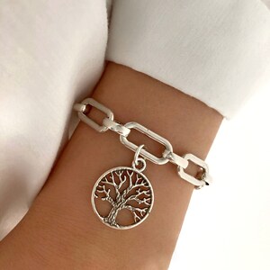Peut inclure: Un bracelet en chaîne argent avec un pendentif arbre de vie. Le pendentif est un cercle avec un motif d'arbre détaillé.