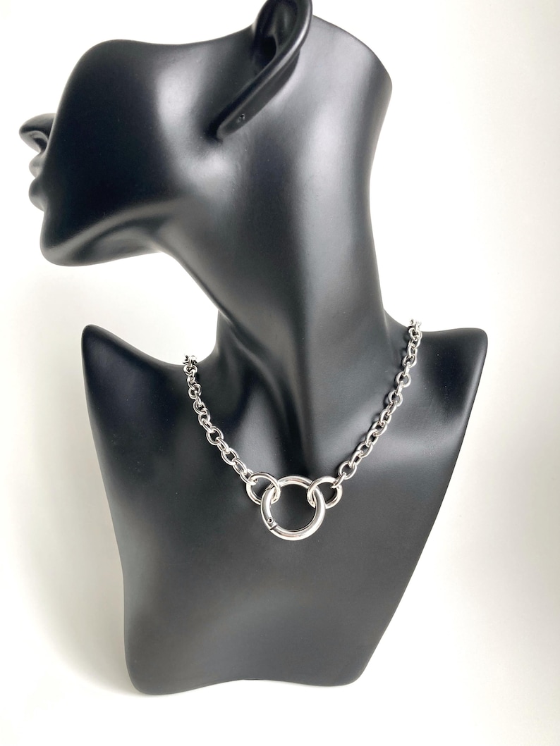 May include: A silver chain necklace with a large, round, silver pendant.