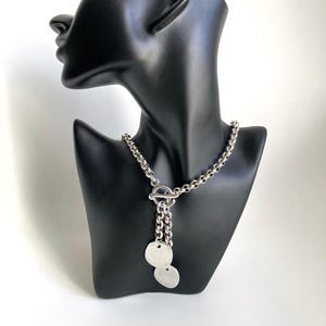 May include: A silver chain necklace with a toggle clasp and two round silver pendants.