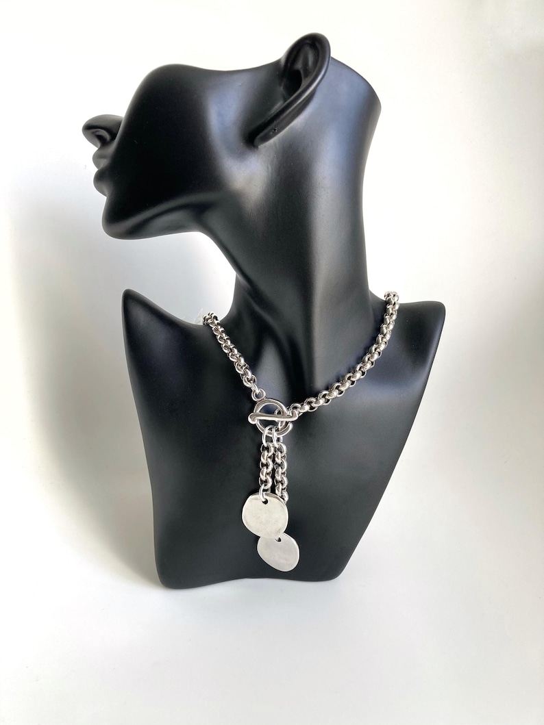 May include: A silver chain necklace with a toggle clasp and two round silver pendants.