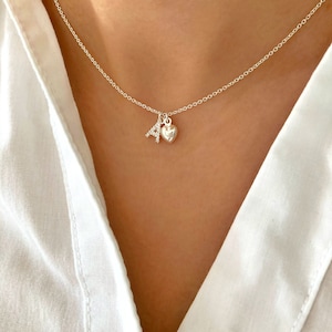 Peut inclure: Un collier en argent avec un petit pendentif en forme de cœur et un pendentif en forme de lettre 'A'. Le pendentif en forme de lettre 'A' est incrusté de petites pierres claires.