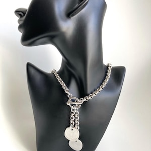 May include: A silver chain necklace with a toggle clasp and two round silver pendants.