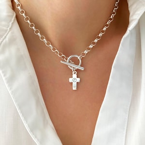 Può includere: Collana color argento con chiusura a leva e piccolo pendente a forma di croce. La croce ha una piccola gemma trasparente al centro. La collana è composta da maglie rotonde.