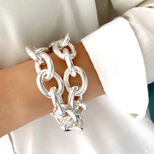 Könnte beinhalten: Ein silbernes, dickes Kettenarmband mit großen ovalen Gliedern. Das Armband wird am Handgelenk getragen.