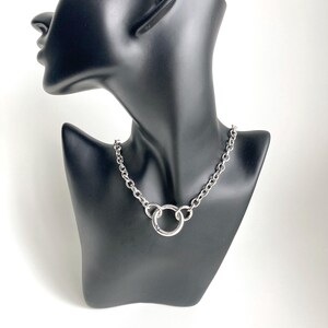 May include: A silver chain necklace with a large, round, silver ring pendant.