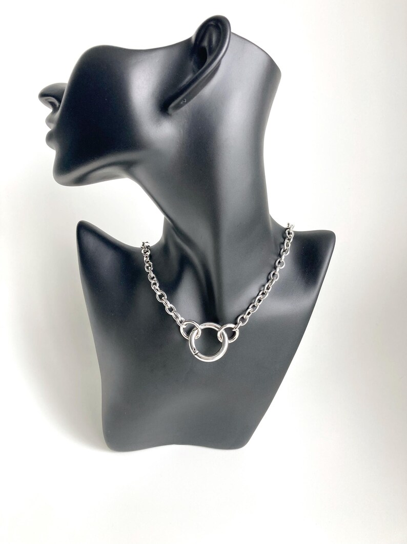 May include: A silver chain necklace with a large, round, silver ring pendant.