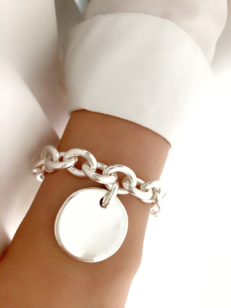 Peut inclure: Un bracelet en argent avec une grosse breloque ronde en argent. Le bracelet est port&eacute; au poignet.