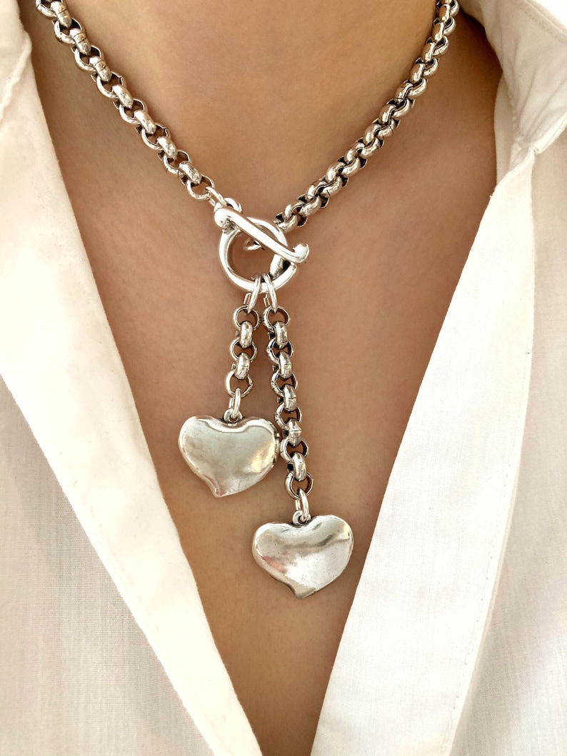 May include: A silver chain necklace with a toggle clasp and two dangling heart charms.