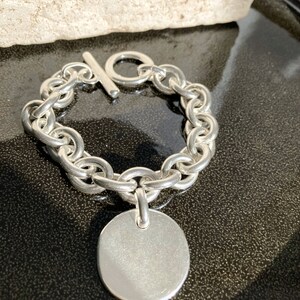 Peut inclure: Un bracelet en argent avec une cha&icirc;ne et un grand pendentif rond en argent. Le bracelet est muni d'un fermoir &agrave; glissi&egrave;re.