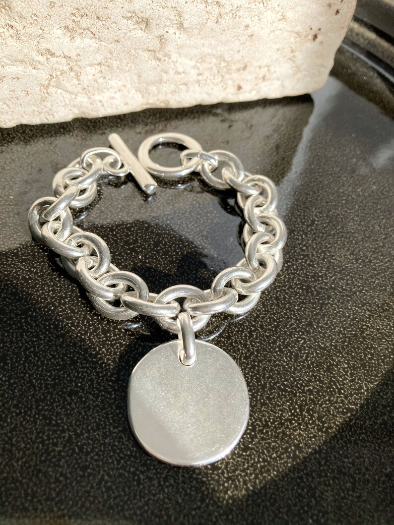 Peut inclure: Un bracelet en argent avec une cha&icirc;ne et un grand pendentif rond en argent. Le bracelet est muni d'un fermoir &agrave; glissi&egrave;re.