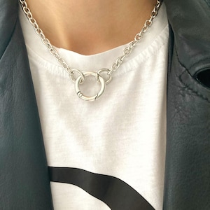 May include: A silver chain necklace with a large, round, silver pendant. The pendant is made of two interlocking circles.