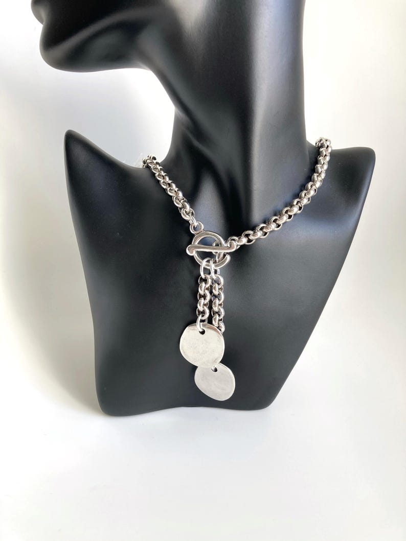 May include: A silver chain necklace with a toggle clasp and two round silver pendants.