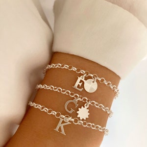 Könnte beinhalten: Drei silberne Kettenarmbänder mit Anhängern. Die Anhänger sind die Buchstaben E, G und K sowie ein kleines Sonnenmotiv.