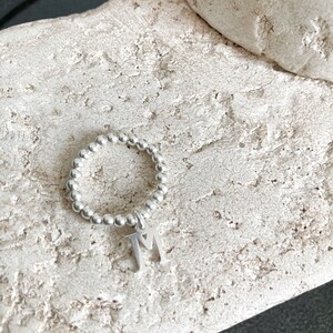 Peut inclure: Un bracelet en argent perlé avec un charme en argent portant les lettres "TM".