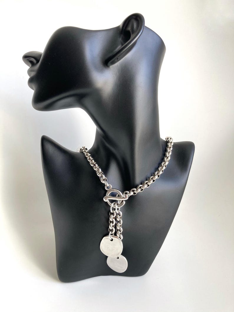 May include: A silver chain necklace with a toggle clasp and two round silver pendants.