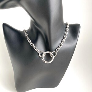 May include: A silver chain necklace with a large, round, silver pendant. The necklace is on a black mannequin.