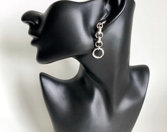 May include: Silver chain earrings with a small circle pendant. The earrings are shown on a black mannequin head.