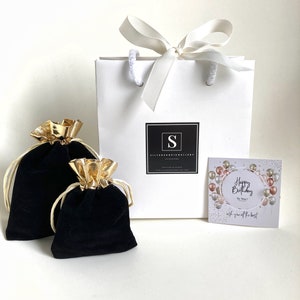 Peut inclure: Un sac cadeau blanc avec un ruban en satin blanc et un logo noir qui dit "S SILVERANDOPALJEWELLERY HANDMADE" avec l'adresse du site Web en dessous. Le sac est pos&eacute; sur une surface blanche avec deux sacs en velours noir &agrave; cordon et une carte qui dit "Joyeux anniversaire &agrave; toi ! Je te souhaite tout le meilleur".