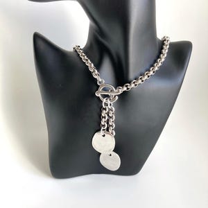 May include: A silver chain necklace with a toggle clasp and two round silver pendants.