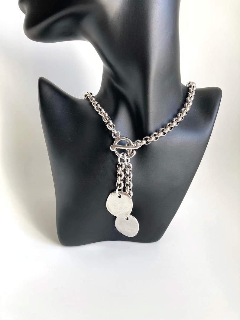 May include: A silver chain necklace with a toggle clasp and two round silver pendants.