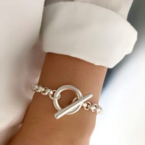 Könnte beinhalten: Ein silbernes Armband mit einem Toggle-Verschluss. Das Armband besteht aus einem Gliederketten-Design.