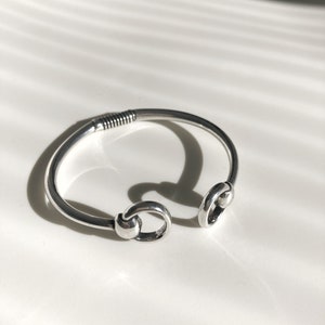 Peut inclure: Un bracelet en argent avec deux éléments décoratifs circulaires ouverts. Le bracelet est fait d'un métal lisse et arrondi.
