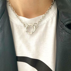 May include: A silver chain necklace with a large, round, silver pendant. The pendant is made of two interlocking circles.