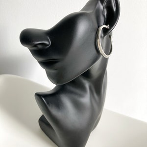 Könnte beinhalten: Ein silberner Creolenohrring an einem schwarzen Mannequin-Kopf.