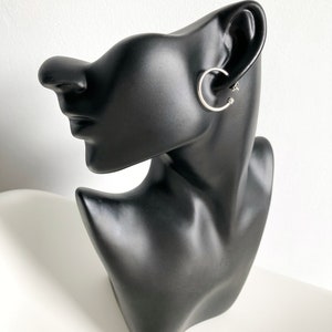 Peut inclure: Une boucle d'oreille en argent sur une tête de mannequin noire. La boucle d'oreille est un simple cercle fin.