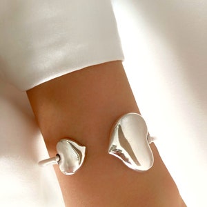 Peut inclure: Bracelet en argent avec deux breloques en forme de cœur. Le plus grand cœur est sur le côté droit du bracelet et le plus petit cœur est sur le côté gauche.