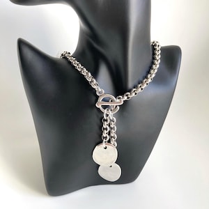 May include: A silver chain necklace with a toggle clasp and two dangling silver discs.