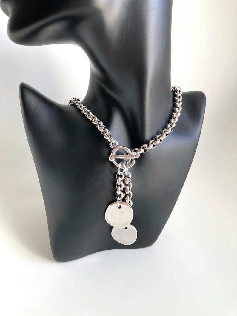 May include: A silver chain necklace with a toggle clasp and two dangling silver discs.