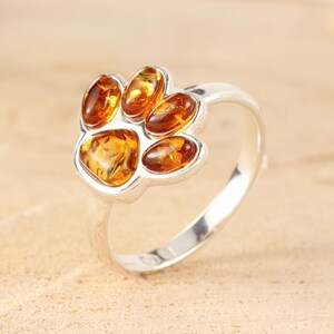 May include: Silver ring with a paw print design featuring amber stones.