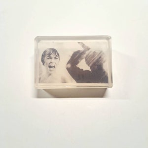 May include: A black and white photo of a person screaming with a shadowy figure behind them. The photo is encased in a clear acrylic block.