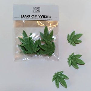 May include: A clear plastic bag with a label that reads "Dark Side Soap Shop" and "Bag of Weed Cannabis & Exotic Spice Scented Soaps". The bag contains several green leaf-shaped soaps. There are also four green leaf-shaped soaps outside of the bag.