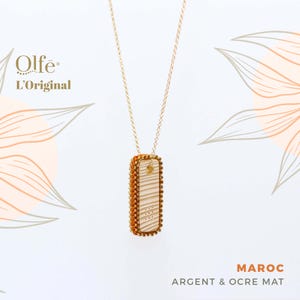 May include: A gold chain necklace with a rectangular pendant. The pendant is made of silver and has a textured, ochre-colored surface. The pendant has the text "MAROC ARGENT & OCRE MAT" on it. The text "Olfé L'Original" is in the top left corner of the image.