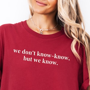 May include: A burgundy t-shirt with rolled-up sleeves. The shirt features the white text: "we don't know-know, but we know." The model is wearing a denim jacket over the shirt.