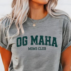 May include: Gray t-shirt with the text "OG MAHA MOMS CLUB" in dark green letters.