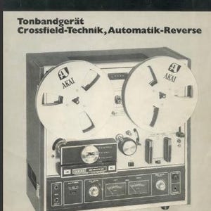 Puede incluir: Un grabador de carrete a carrete Akai X-201-D negro con tres cabezales de cinta, tres motores y reversa automática. El grabador tiene una placa frontal plateada con un logotipo Akai plateado y un panel de control plateado con perillas y botones.