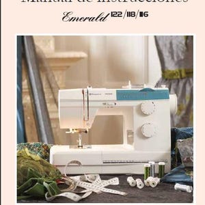 May include: A white sewing machine with a blue top and a needle threaded with white thread. The machine is sitting on a table with a green fabric and a measuring tape. The text "Emerald 122/118/116" is visible on the front of the machine.