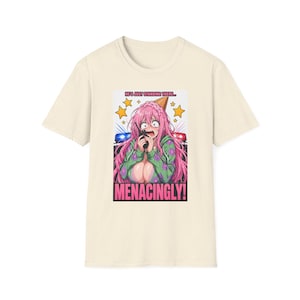 May include: Cream-colored t-shirt featuring a colorful anime-style graphic. The graphic depicts a surprised character with pink hair, holding a phone, with the text "HE'S JUST STANDING THERE... MENACINGLY!" above and below the character.